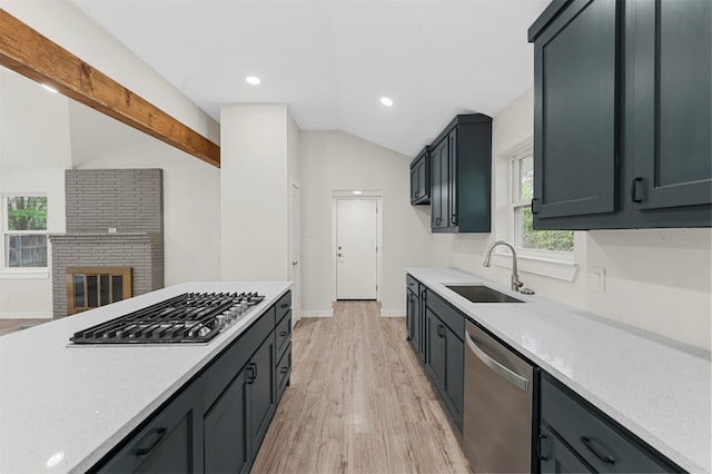 kitchen with appliances with stainless steel finishes, vaulted ceiling, sink, a fireplace, and light hardwood / wood-style floors