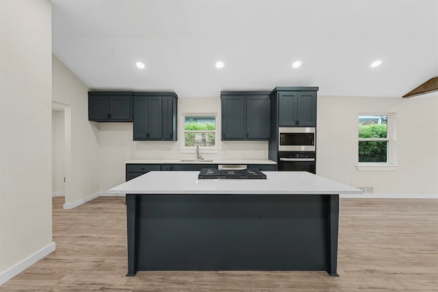 kitchen with a healthy amount of sunlight, a kitchen island, light wood-type flooring, and sink