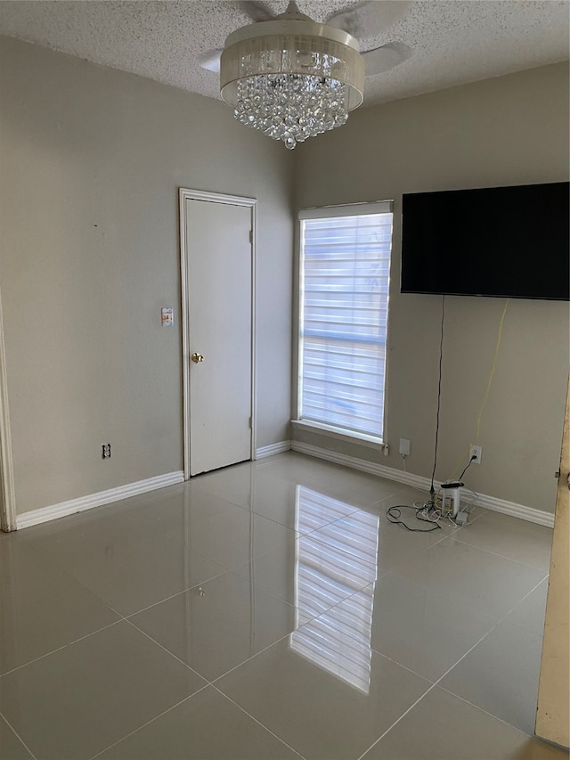 tiled empty room featuring a textured ceiling and a notable chandelier