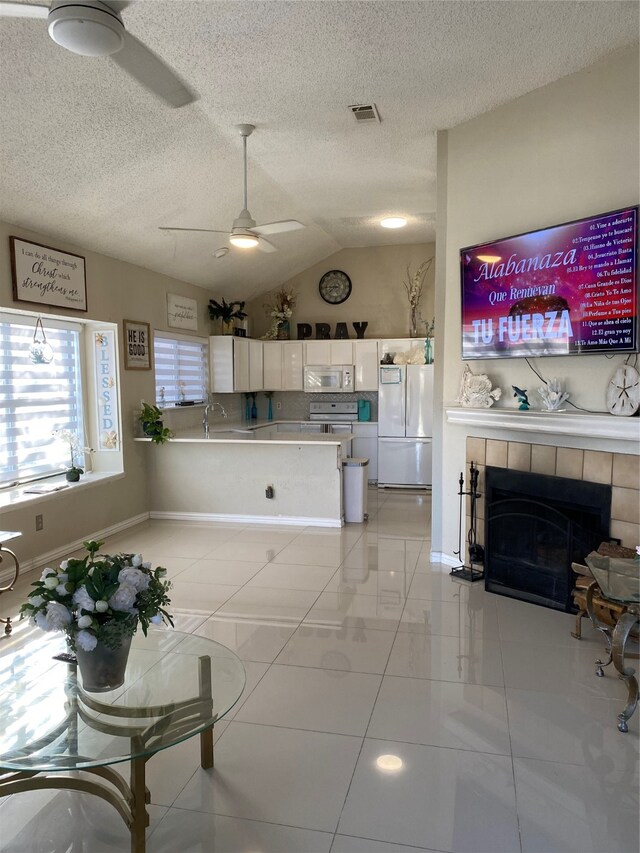 kitchen featuring white appliances, vaulted ceiling, ceiling fan, a fireplace, and white cabinetry