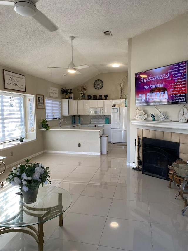 710 Cresent Dr, Desoto, TX 75115 - living room featuring ceiling fan, vaulted ceiling, a tiled fireplace, light tile patterned floors, and a textured ceiling