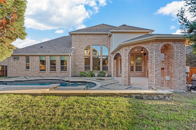 rear view of property featuring a lawn, a swimming pool with hot tub, and a patio area