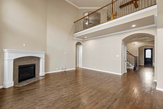 unfurnished living room with crown molding, a tile fireplace, dark wood-type flooring, and a high ceiling