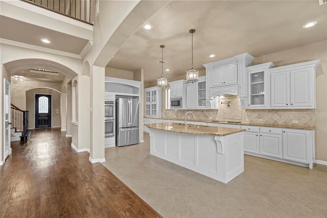 kitchen with a kitchen island with sink, white cabinets, light stone countertops, light hardwood / wood-style floors, and stainless steel appliances