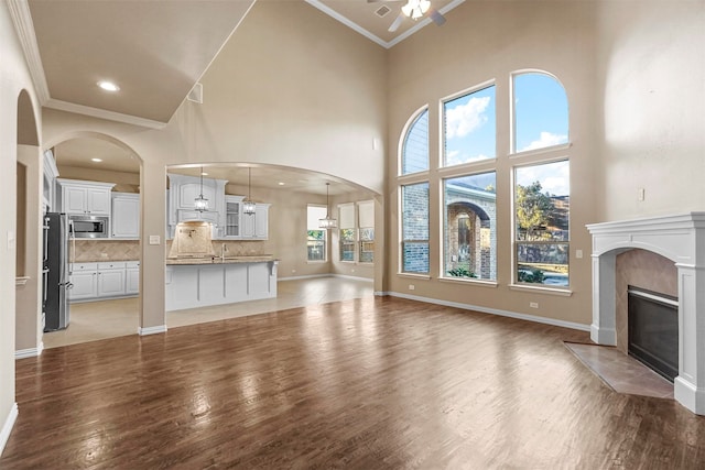 unfurnished living room with ceiling fan, ornamental molding, a high ceiling, and hardwood / wood-style flooring