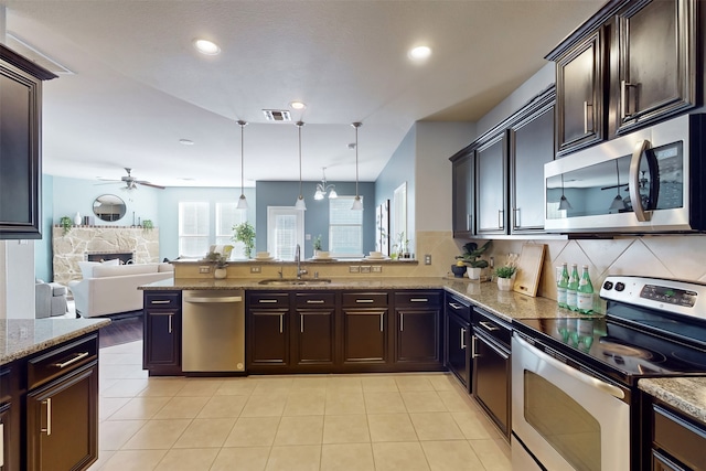 kitchen featuring sink, a stone fireplace, pendant lighting, ceiling fan with notable chandelier, and appliances with stainless steel finishes