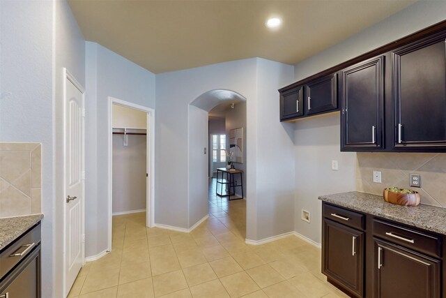 kitchen featuring dark brown cabinets, light stone counters, light tile patterned floors, and tasteful backsplash