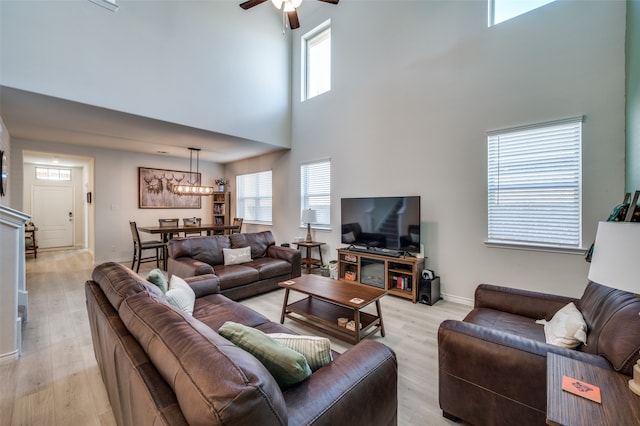 living room with ceiling fan, light hardwood / wood-style flooring, and a towering ceiling