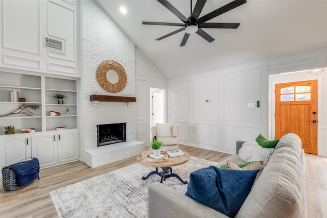 living room with a fireplace, built in shelves, light wood-type flooring, and ceiling fan