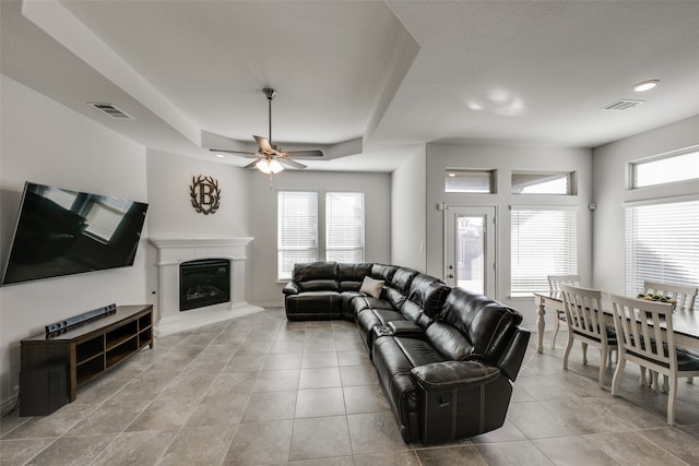 tiled living room with a tray ceiling, ceiling fan, and a healthy amount of sunlight