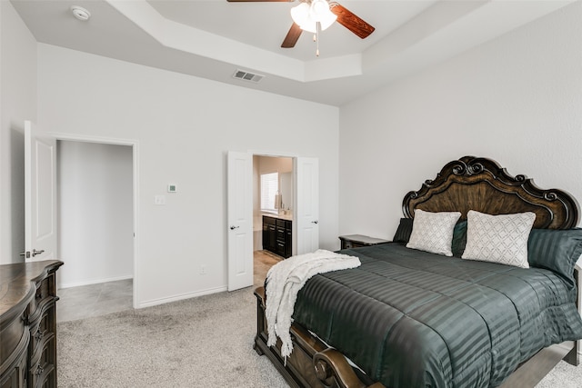 carpeted bedroom featuring ensuite bathroom, ceiling fan, and a raised ceiling