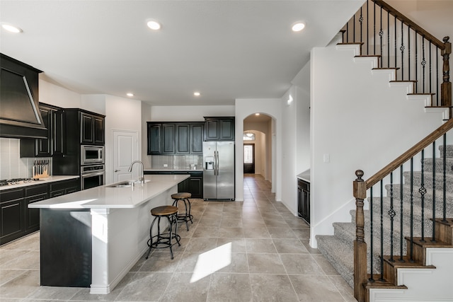 kitchen featuring a breakfast bar, a kitchen island with sink, sink, decorative backsplash, and appliances with stainless steel finishes