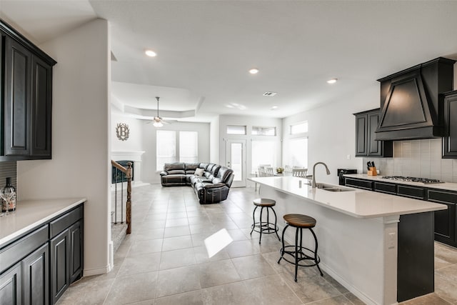 kitchen with custom exhaust hood, a center island with sink, sink, decorative backsplash, and a kitchen bar