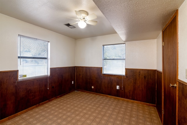 unfurnished room featuring ceiling fan, wood walls, and a textured ceiling