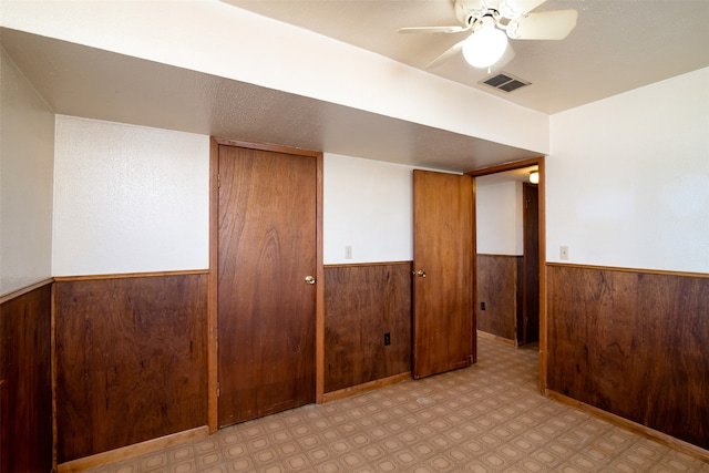 basement with ceiling fan and wooden walls