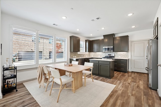 kitchen with decorative backsplash, light wood-type flooring, dark brown cabinets, a kitchen island, and stainless steel appliances