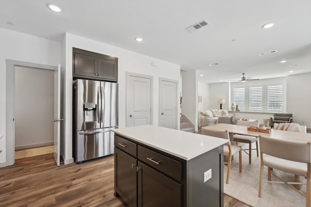 kitchen with dark brown cabinetry, ceiling fan, dark hardwood / wood-style flooring, stainless steel refrigerator with ice dispenser, and a kitchen island