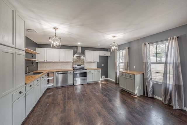 kitchen featuring wood counters, appliances with stainless steel finishes, wall chimney exhaust hood, decorative light fixtures, and white cabinetry