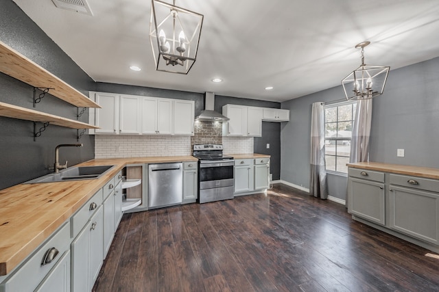 kitchen with wood counters, stainless steel appliances, sink, wall chimney range hood, and decorative light fixtures