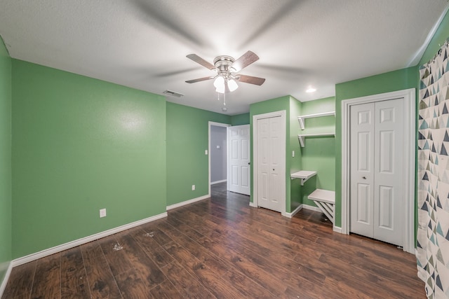 unfurnished bedroom featuring ceiling fan, dark hardwood / wood-style flooring, a textured ceiling, and two closets