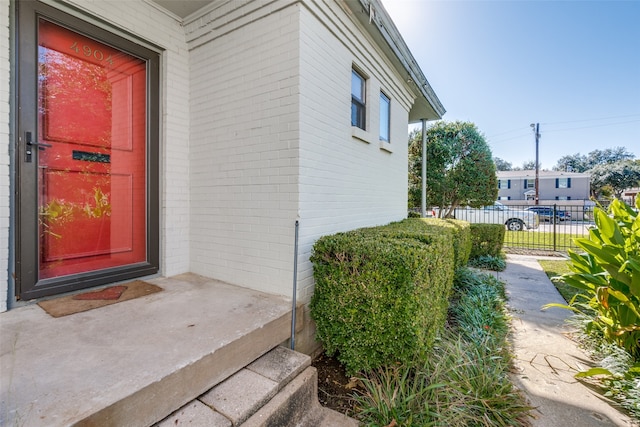 view of exterior entry with brick siding and fence