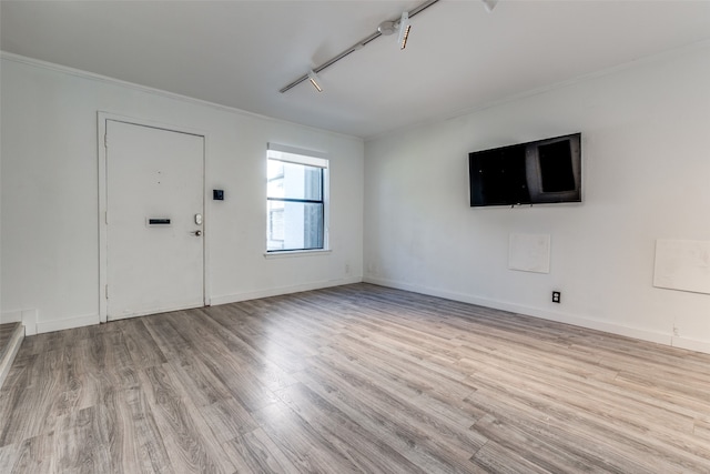 unfurnished living room with baseboards, wood finished floors, rail lighting, and crown molding