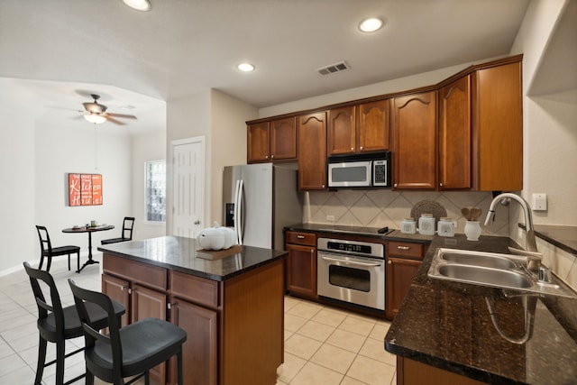 kitchen with a center island, sink, decorative backsplash, ceiling fan, and appliances with stainless steel finishes