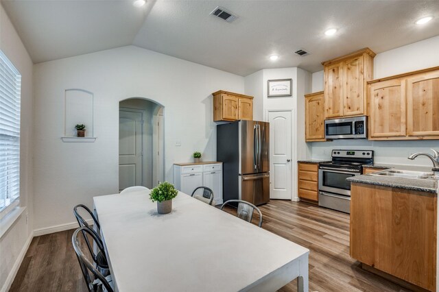 kitchen featuring sink, hardwood / wood-style floors, lofted ceiling, light brown cabinetry, and appliances with stainless steel finishes