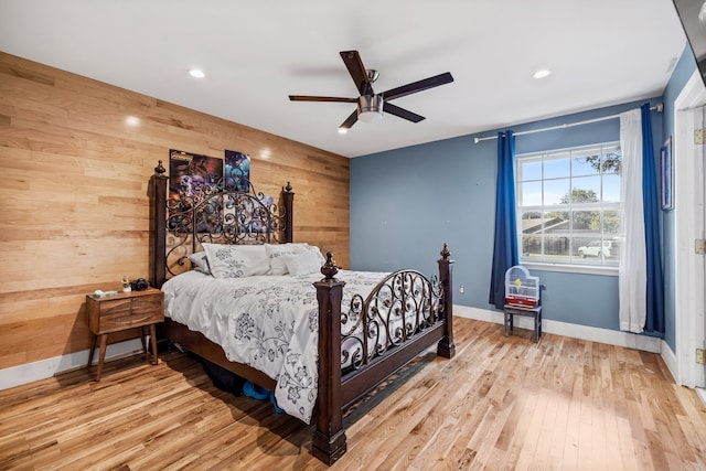 bedroom with light wood-type flooring, ceiling fan, and wooden walls