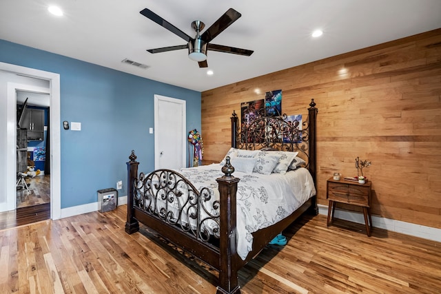 bedroom featuring ceiling fan, wood-type flooring, and wood walls