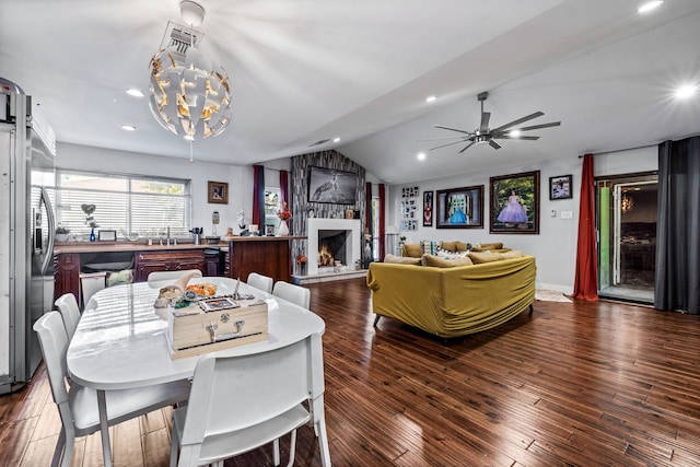 dining space featuring a fireplace, ceiling fan with notable chandelier, dark wood-type flooring, and lofted ceiling