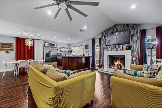 living room featuring vaulted ceiling, dark wood-type flooring, ceiling fan with notable chandelier, and a large fireplace