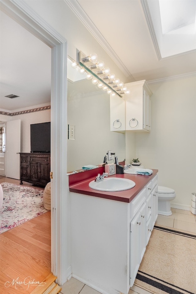 bathroom with a skylight, ornamental molding, vanity, wood-type flooring, and toilet