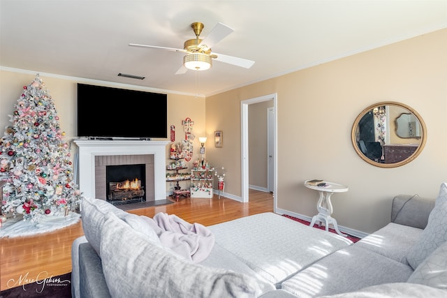 living room with hardwood / wood-style flooring, ceiling fan, crown molding, and a brick fireplace