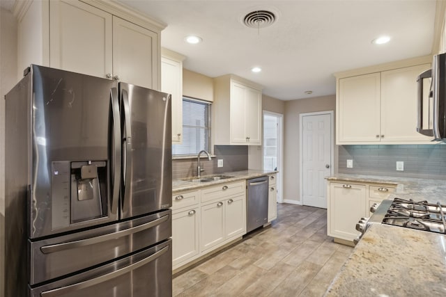 kitchen with tasteful backsplash, light stone counters, stainless steel appliances, sink, and light hardwood / wood-style flooring