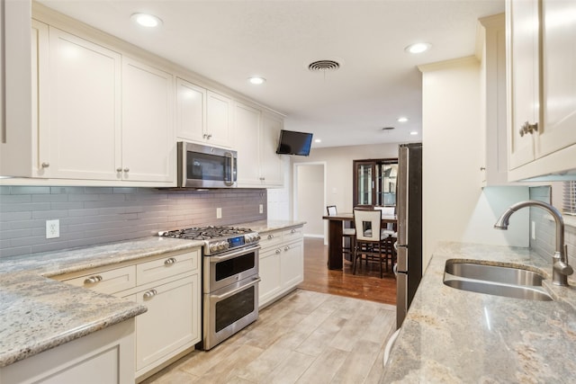 kitchen featuring light stone countertops, sink, stainless steel appliances, backsplash, and light wood-type flooring