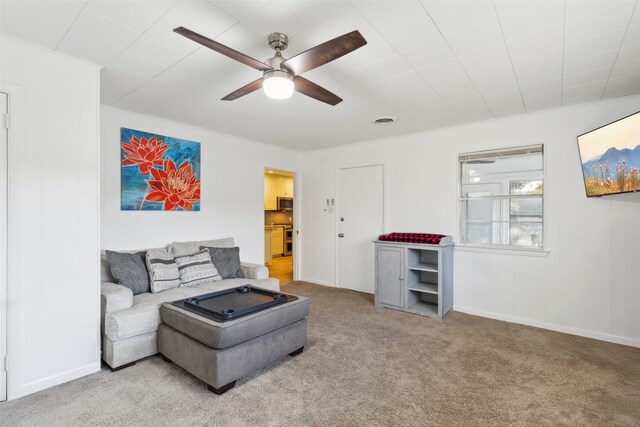 living room with ceiling fan, crown molding, and light colored carpet