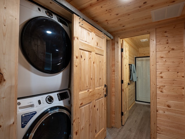 laundry area with wood walls, light wood-type flooring, stacked washer / dryer, and wood ceiling