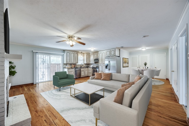 living room featuring ceiling fan, sink, light wood-type flooring, a textured ceiling, and ornamental molding