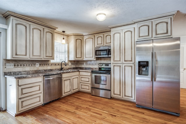 kitchen featuring sink, hanging light fixtures, a textured ceiling, appliances with stainless steel finishes, and light wood-type flooring