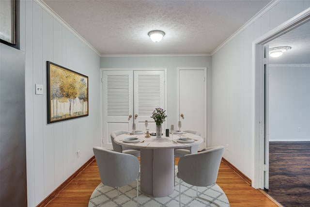 dining room with a textured ceiling, light hardwood / wood-style flooring, and ornamental molding