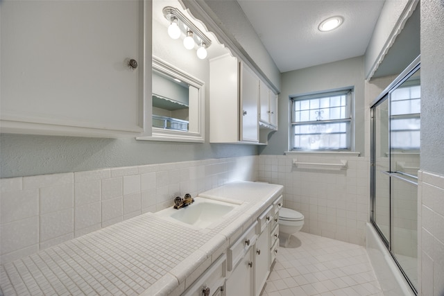 full bathroom with tile patterned floors, a textured ceiling, toilet, shower / bath combination with glass door, and tile walls