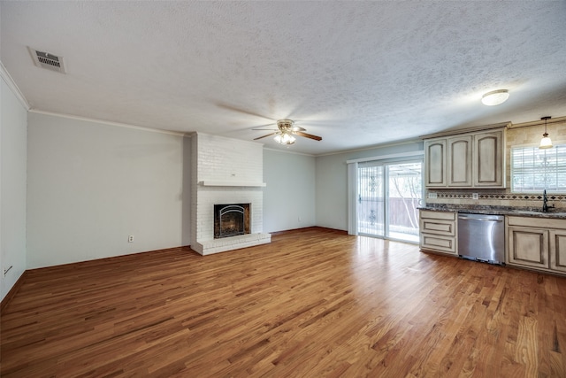 kitchen with ceiling fan, dishwasher, a brick fireplace, a textured ceiling, and hardwood / wood-style flooring