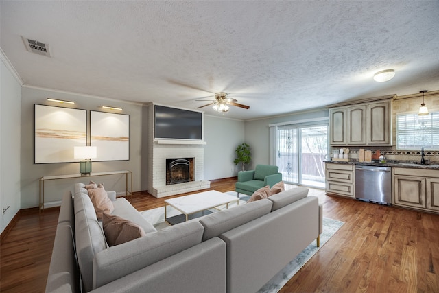 living room featuring sink, light hardwood / wood-style flooring, ceiling fan, a textured ceiling, and a fireplace