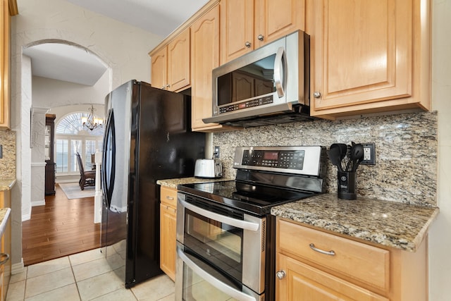 kitchen with light stone countertops, stainless steel appliances, light brown cabinetry, a notable chandelier, and light tile patterned floors