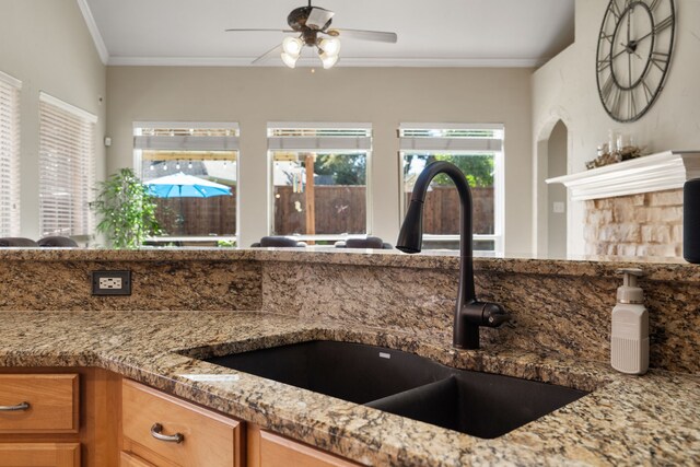 kitchen with light stone countertops, ceiling fan, crown molding, and sink