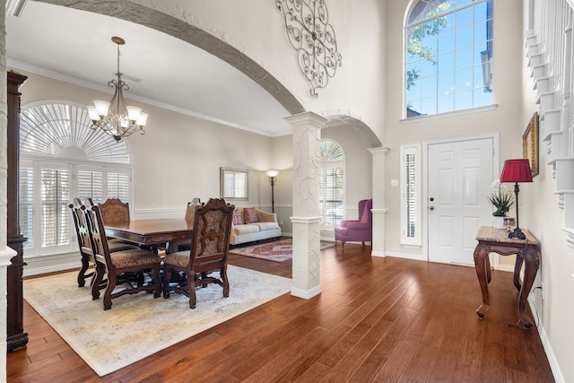 dining room with wood-type flooring, an inviting chandelier, decorative columns, and crown molding