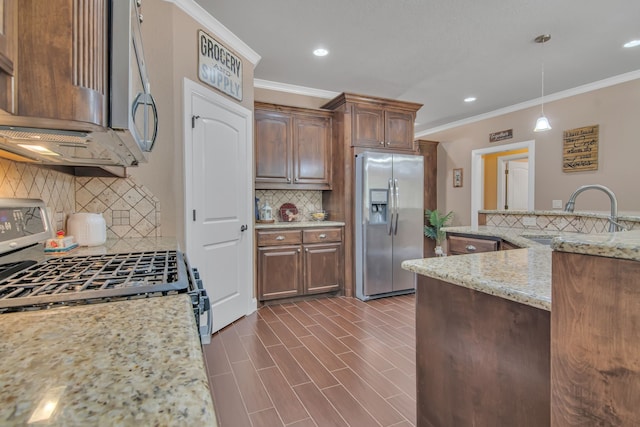 kitchen with light stone countertops, appliances with stainless steel finishes, backsplash, sink, and hanging light fixtures