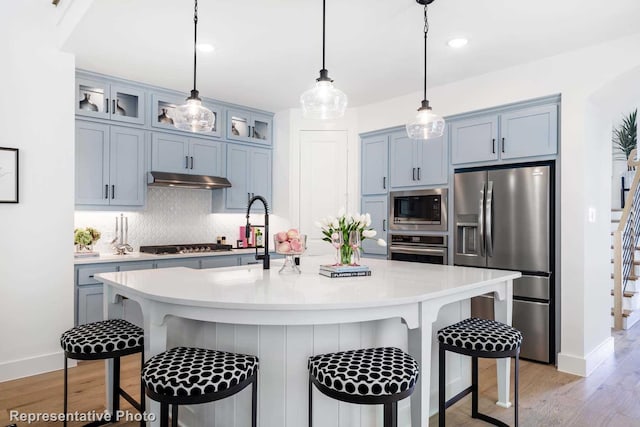 kitchen with a breakfast bar area, hanging light fixtures, light hardwood / wood-style floors, and appliances with stainless steel finishes