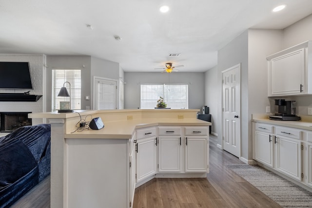 kitchen with a brick fireplace, ceiling fan, light hardwood / wood-style flooring, a center island, and white cabinetry